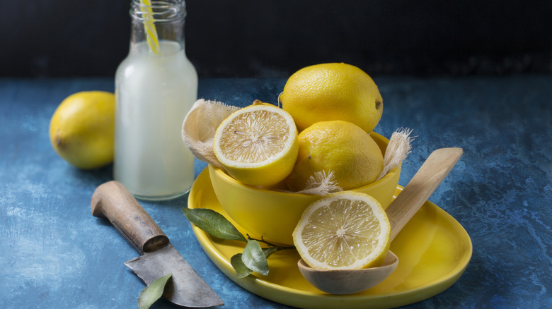 Yellow bowlful of sliced lemons next to knife and bottle of lemon juice