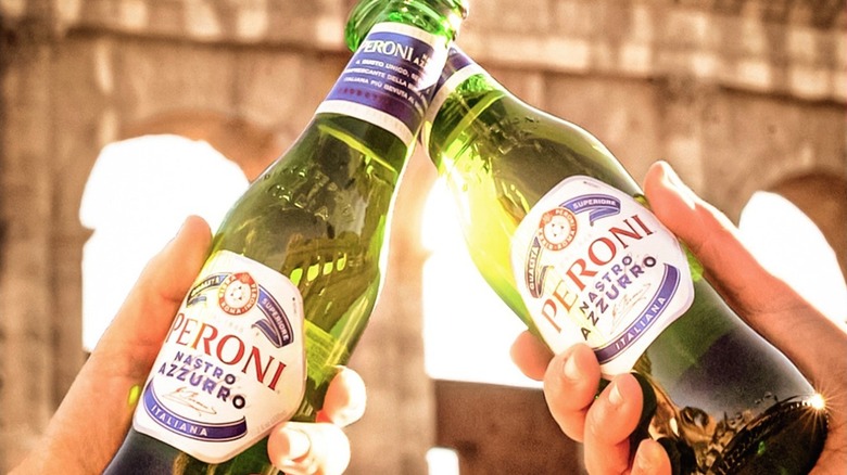 Two bottles of Peroni being clinked together with the Colosseum in the background