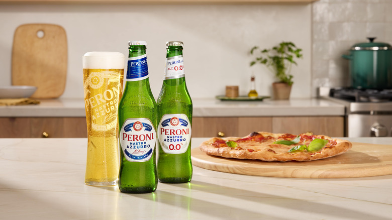 Two bottles of Peroni placed on a countertop beside a glass and pizza