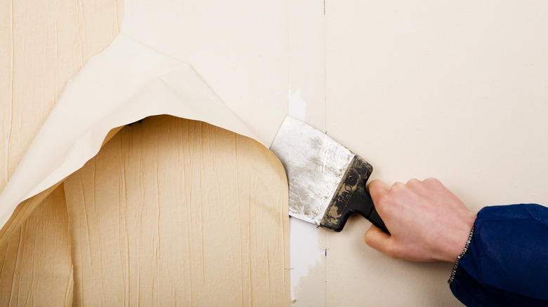 Hand removing old beige and textured wallpaper with a spatula