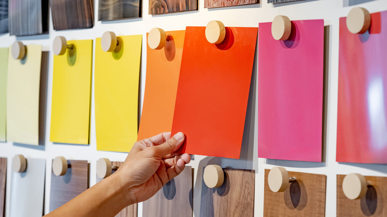 Hand picking material swatch from wall with many colorful swatches pinned on the wall