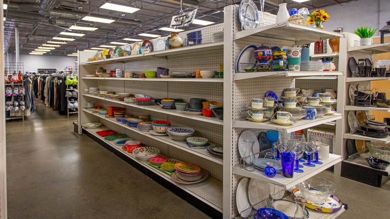Kitchen items on the shelves of a thrift store including plates and cups